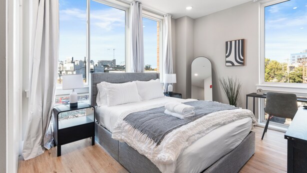 Ein modernes Schlafzimmer mit einem großen Bett, einem Schreibtisch und Blick auf die Stadt.