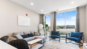 Ein modernes Wohnzimmer mit einer Couch, Sesseln, einem Couchtisch und einem großen Fenster mit Blick auf die Stadt.
