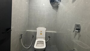 Un bany petit i modern amb un vàter blanc, una dutxa i un assecador de mans.