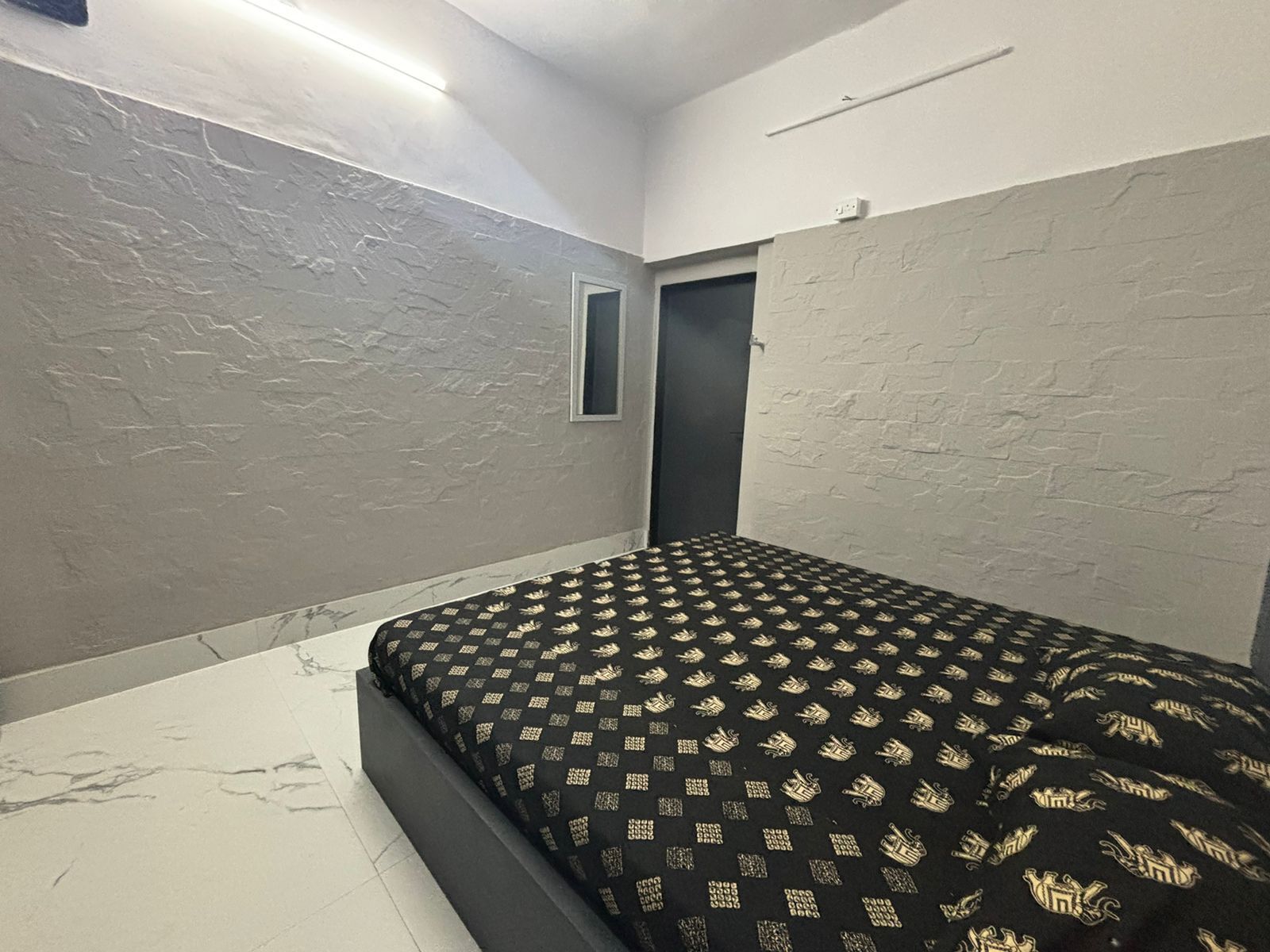 Een kamer met een bed, een deur en een klein raam.