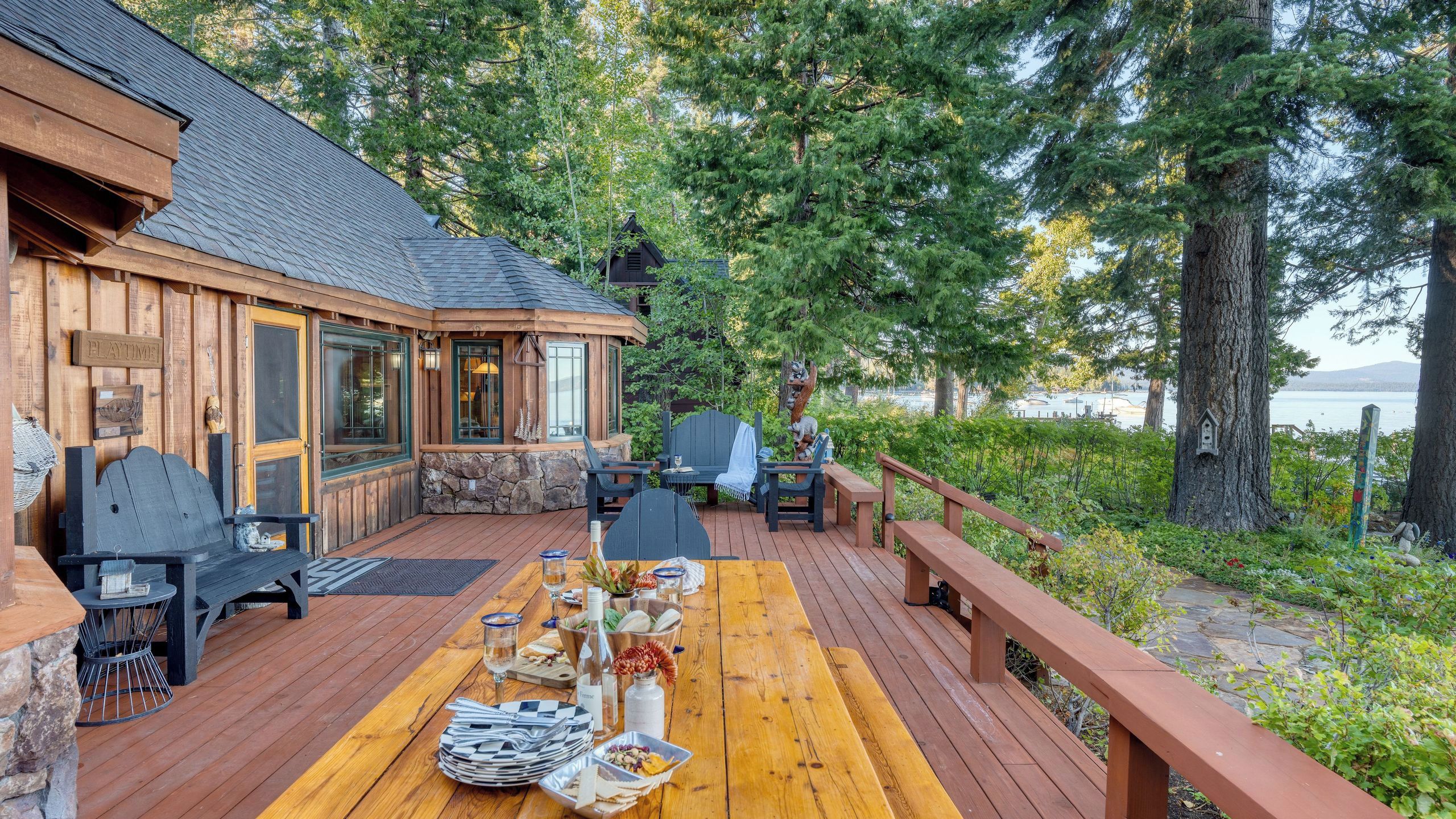 A wooden deck with a table set for dining, surrounded by stone walls and large windows.