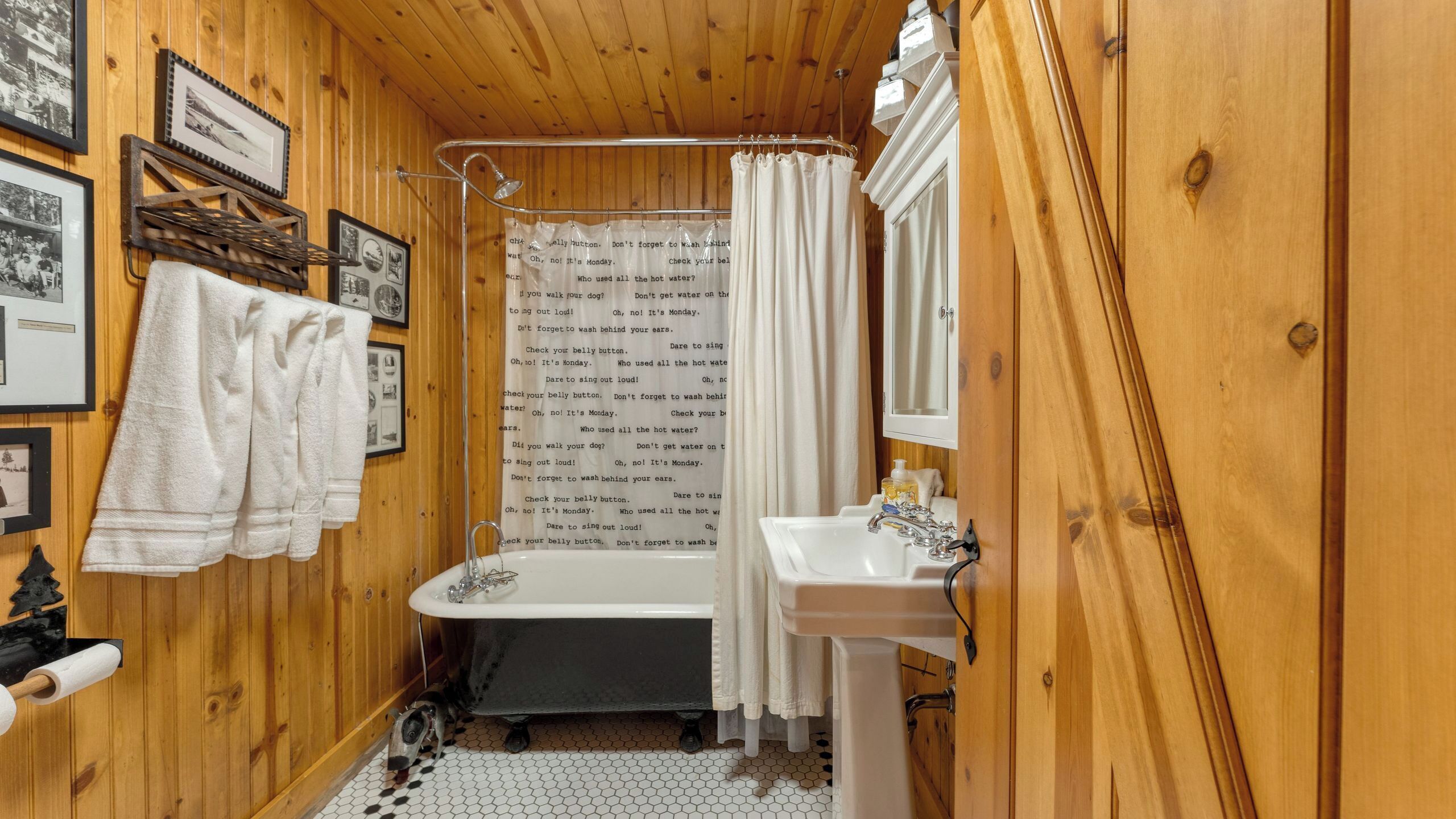 A wooden bathroom with a bathtub, a sink, and a shower curtain with text.