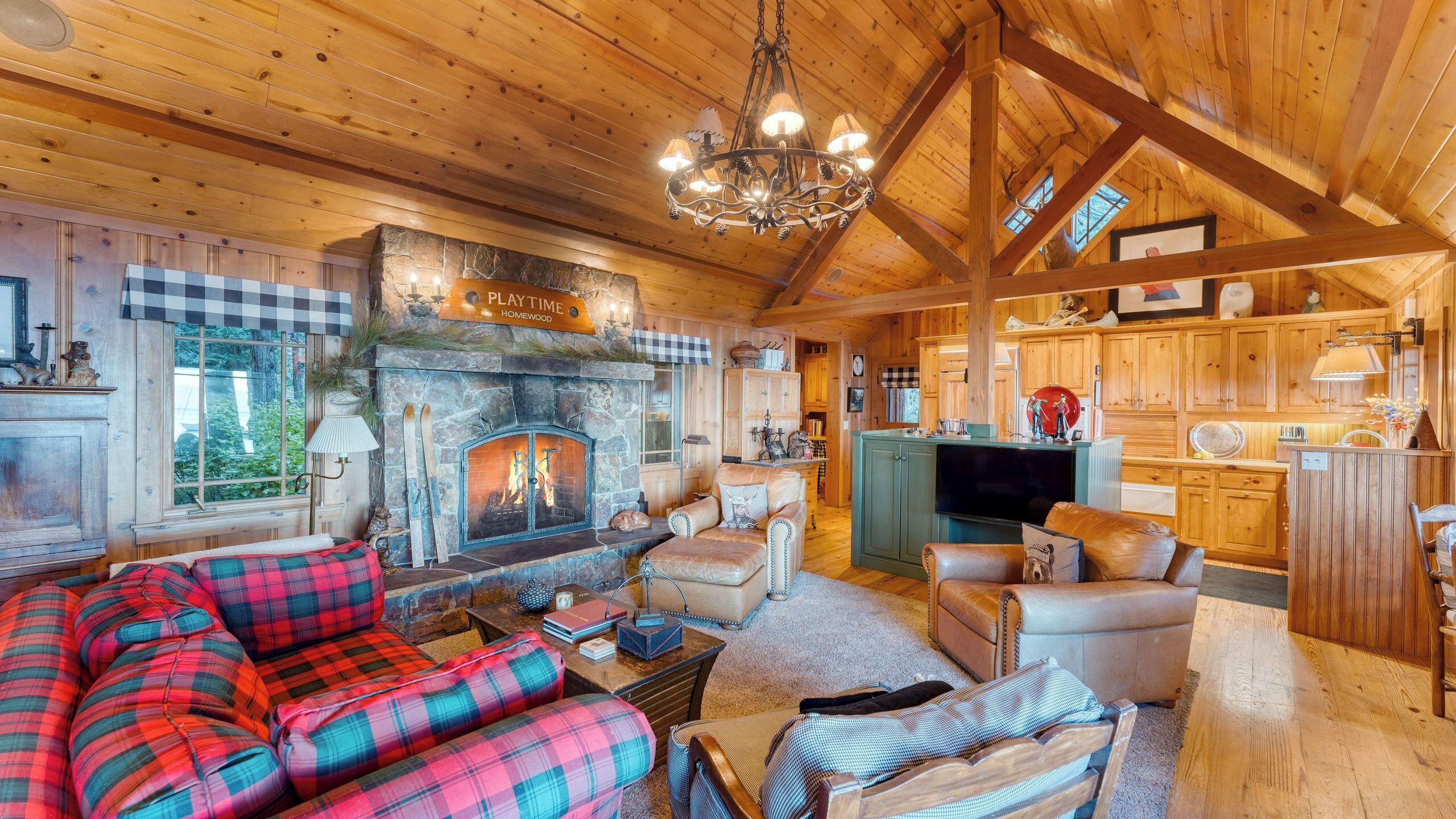 L’intérieur chaleureux d’un chalet avec une cheminée en pierre, des meubles à motifs écossais, un téléviseur et des meubles en bois.