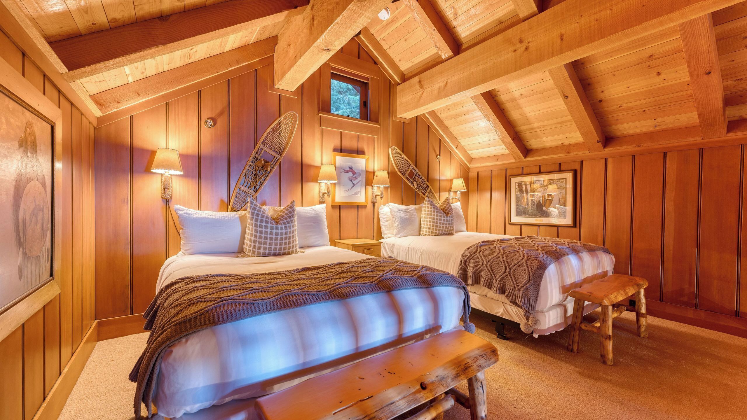 A wooden cabin bedroom with two beds, a bench, and a small table.
