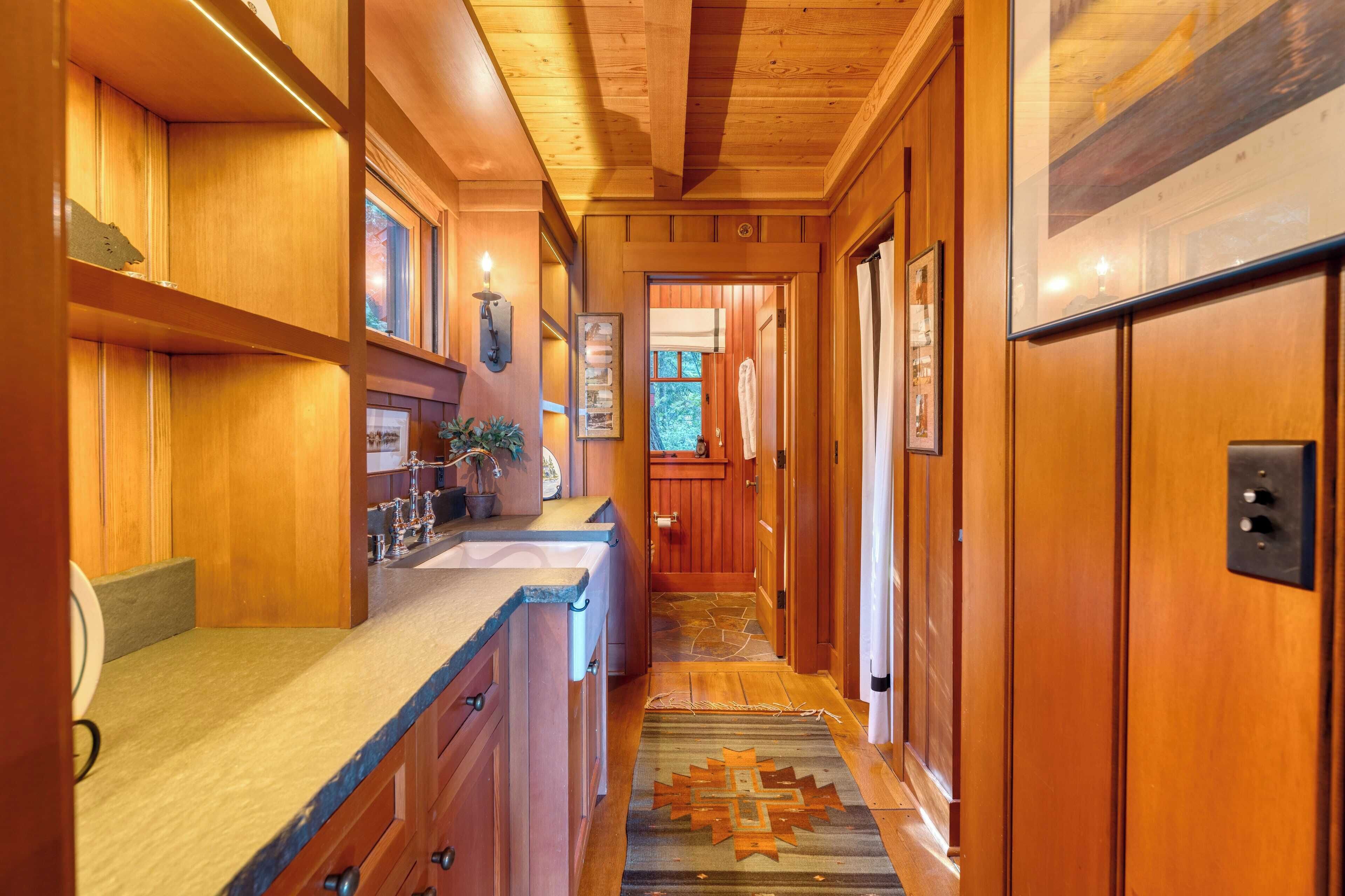 A wooden interior hallway with a kitchen area, wooden cabinets, a rug, and a door leading to another room.