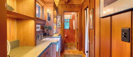A wooden interior hallway with a kitchen area, wooden cabinets, a rug, and a door leading to another room.