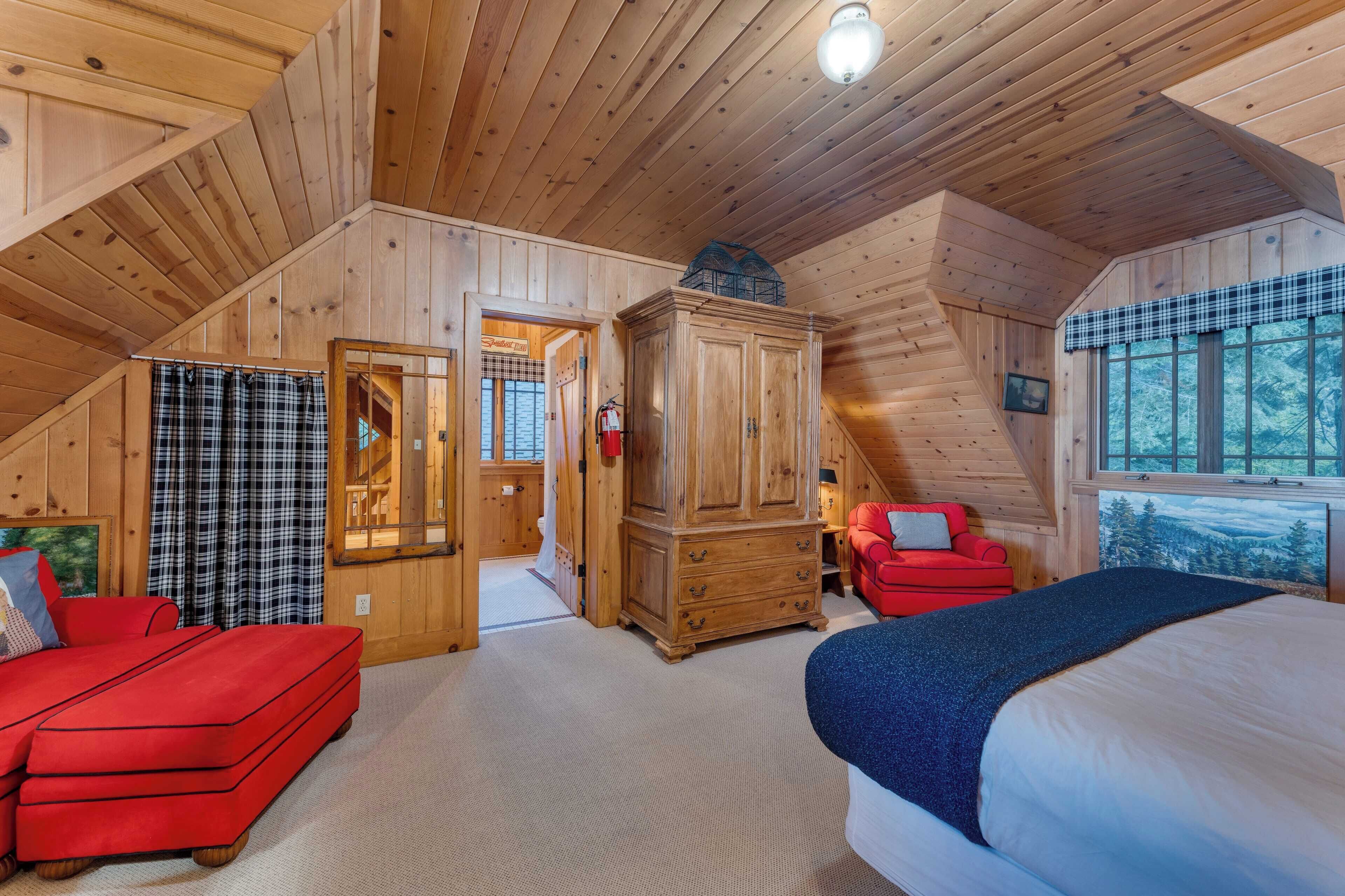 A cozy cabin room with a loft bed, a red sofa, a wooden cabinet, and a plaid curtain.