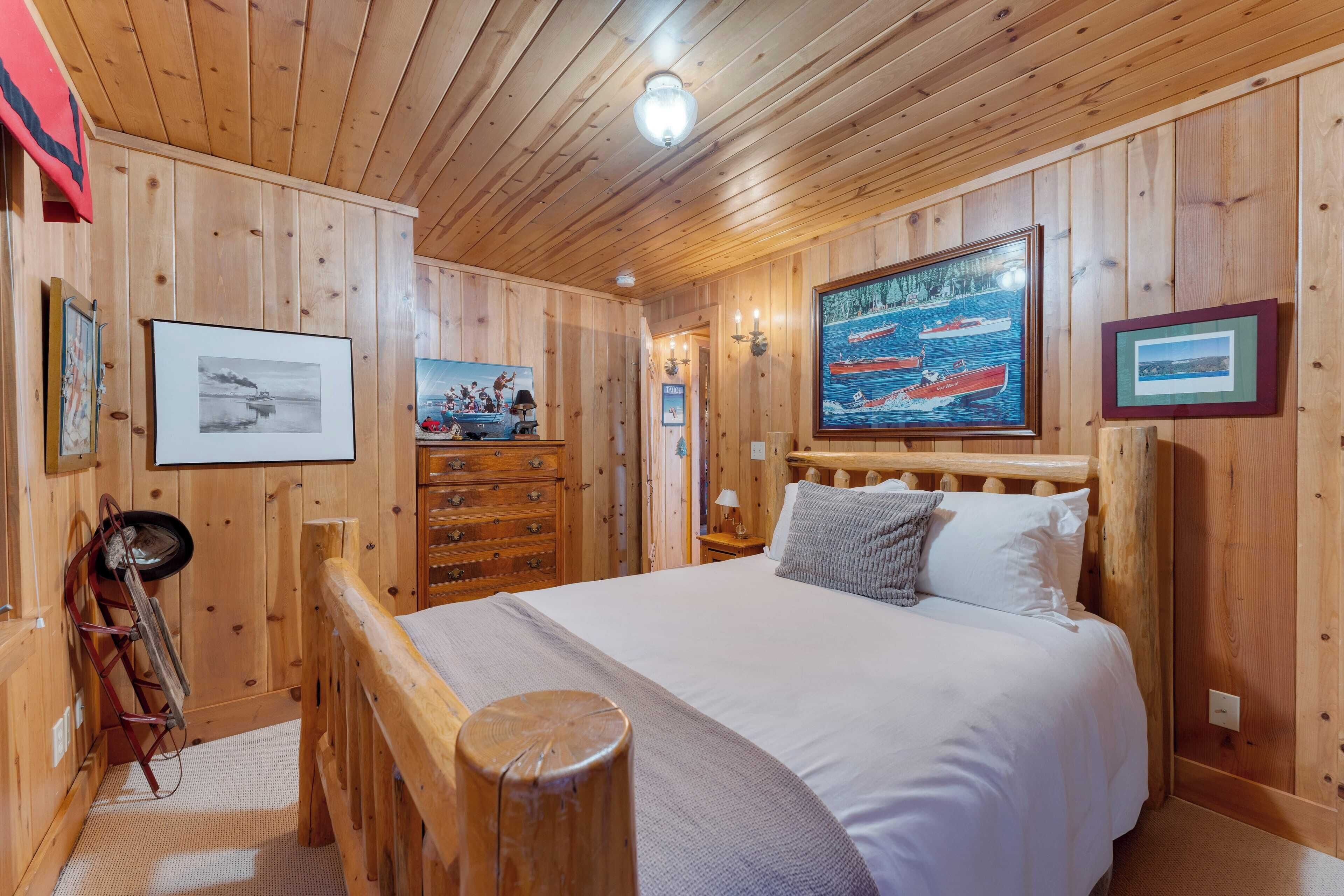 A wooden-paneled room with a bed, dresser, and artwork on the walls.