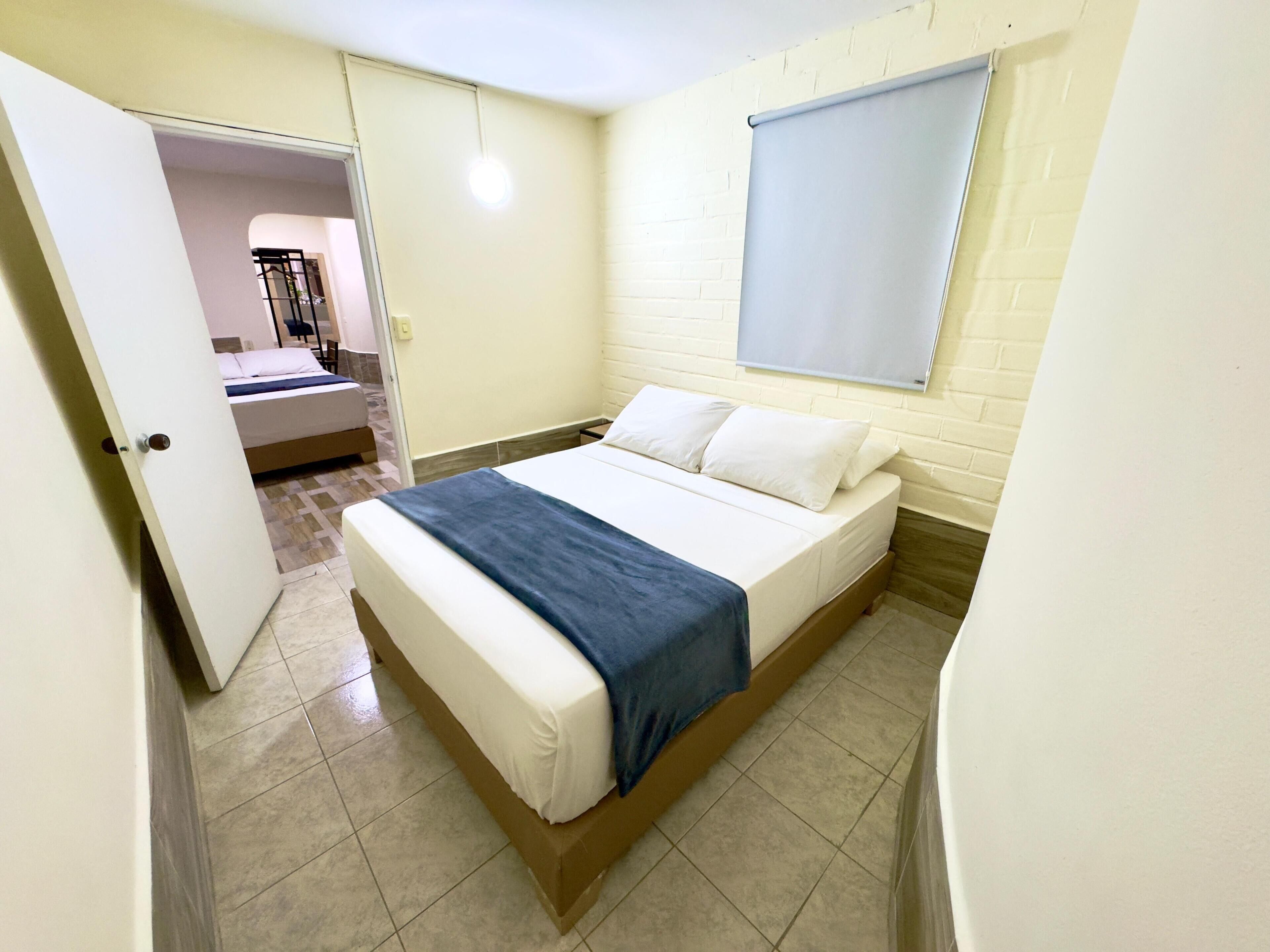 Un dormitorio con cama, ventana con persianas, puerta y suelo de baldosas.