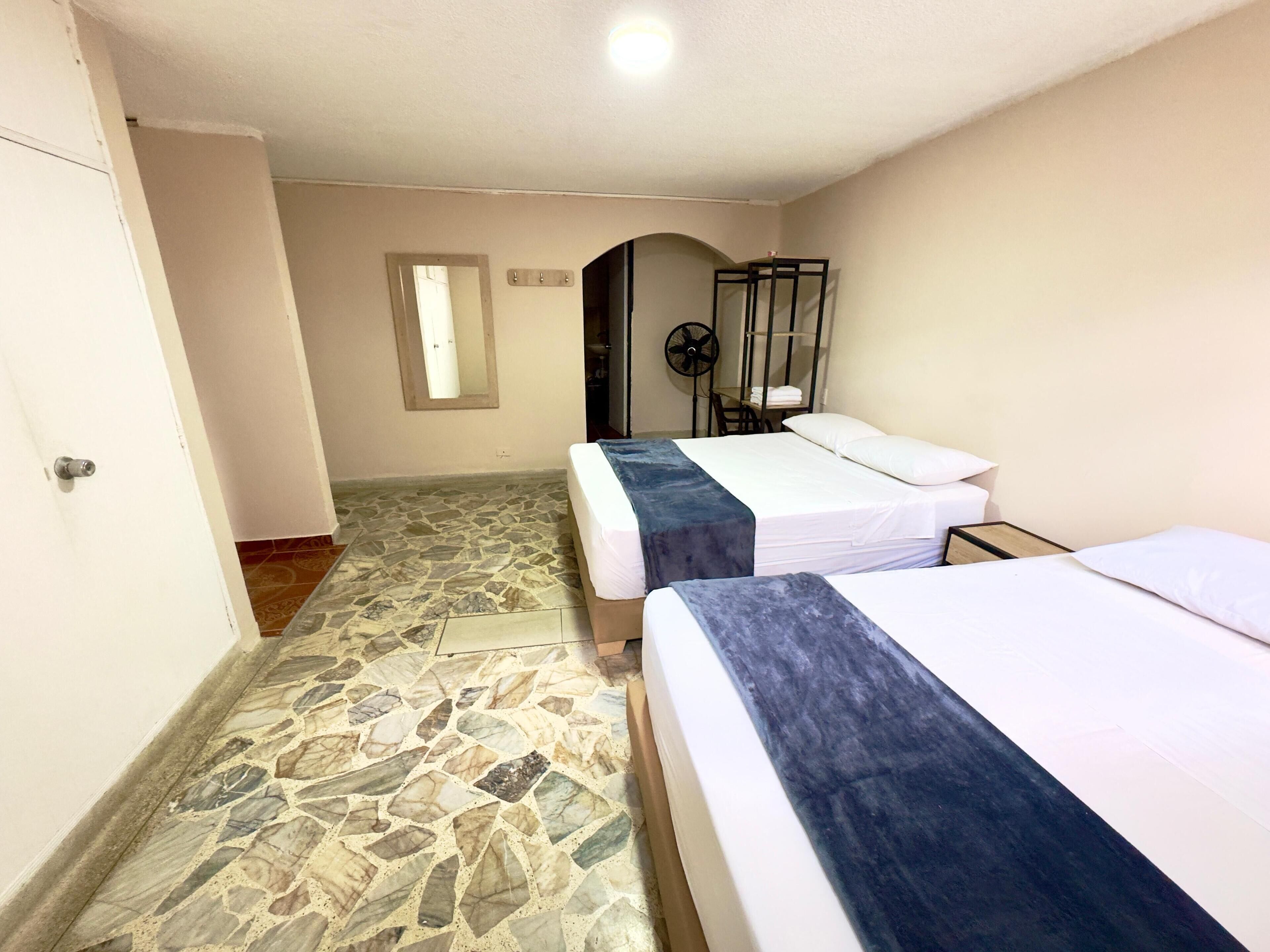 A hotel room with two beds, a stone floor, a fan, and a mirror on the wall.