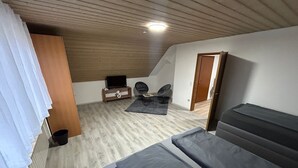 A bedroom with a sloped ceiling, a bed, a TV on a stand, a chair, and a small table. - Vacation apartment zur Linde II (Altertheim)