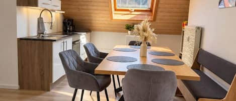 A modern kitchen with wooden cabinets, a dining area with a wooden table and chairs, and a skylight above the table.