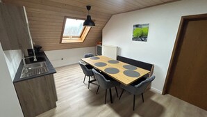 A compact kitchen with a dining area, featuring a wooden table with circular cutouts, grey chairs, and a skylight above the sink. - Vacation apartment zur Linde II (Altertheim)