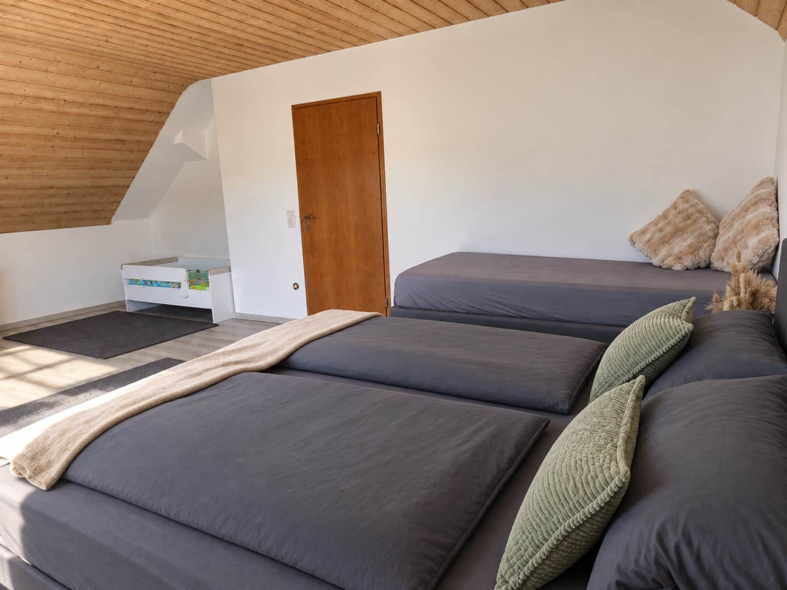 A bedroom with a sloped ceiling, a wooden door, and a bed with multiple pillows.