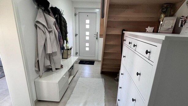 A hallway with a white dresser, a coat rack with coats, and a wooden staircase. - Vacation apartment zur Linde II (Altertheim)