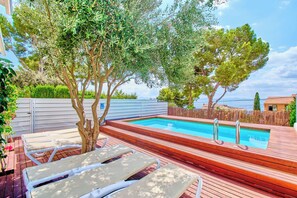 A swimming pool with wooden deck and lounge chairs, surrounded by trees and a fence. - Sea Dreams Apartment with sea View, private pool, Wifi, AACC, BBQ (Alcudia)
