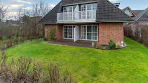 A two-story house with a balcony, brick exterior, and a grassy yard. - Ferienwohnung in St. Peter-ording (St. Peter-Ording)