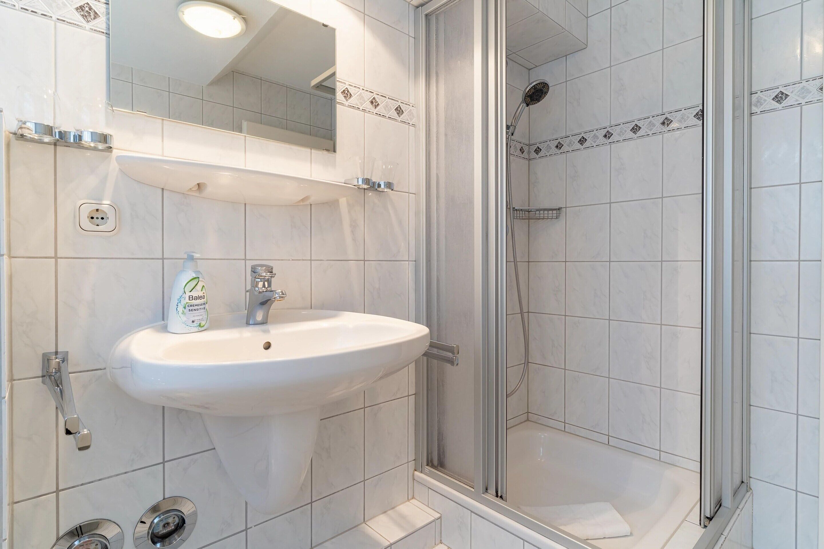 A bathroom with a white sink, a mirror, and a glass-enclosed shower.