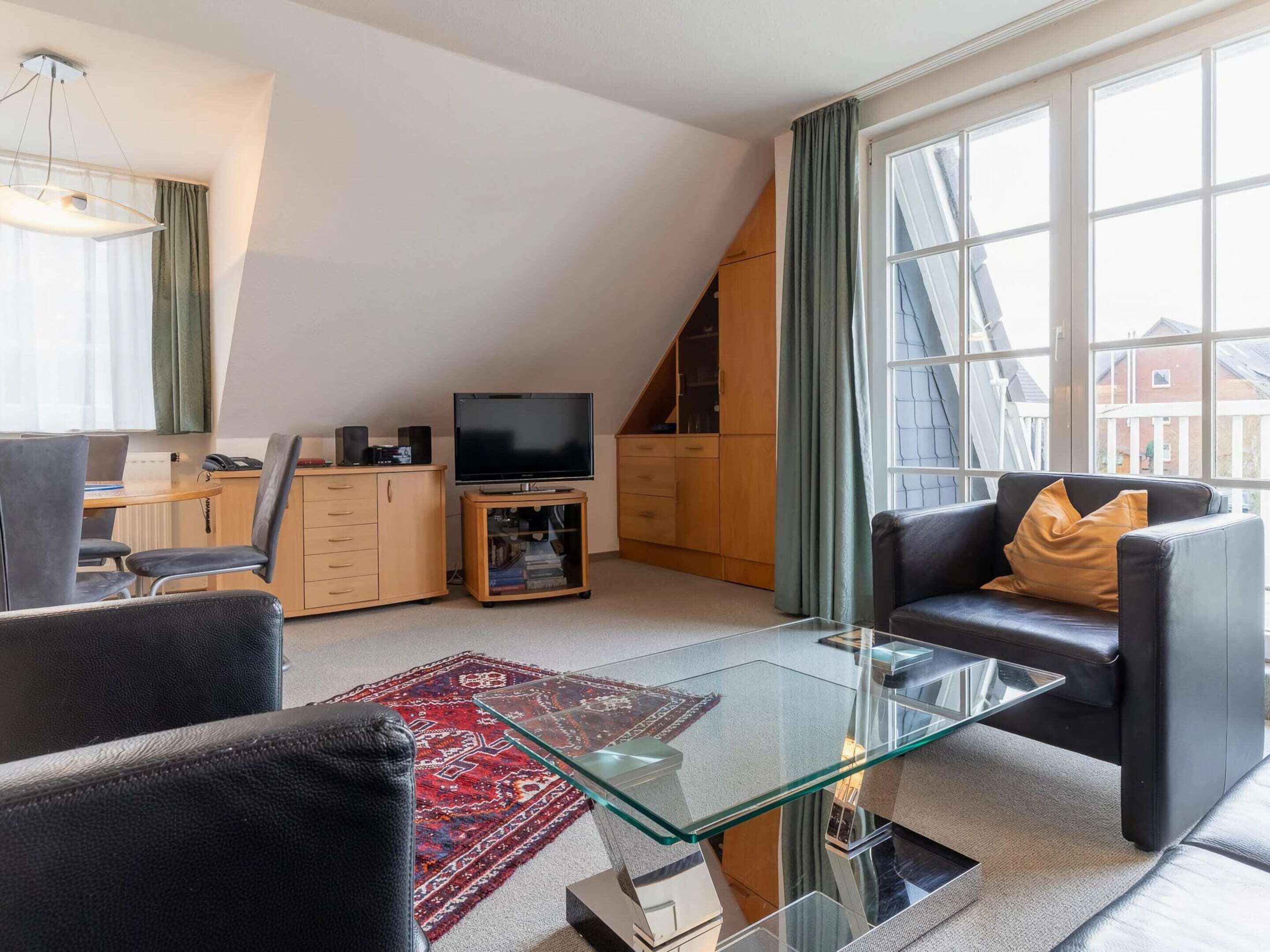 Un salon moderne avec une table basse en verre, un canapé en cuir noir et un téléviseur posé sur un meuble en bois.