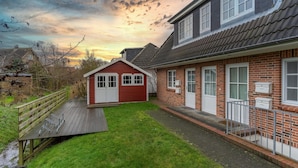 A residential property with a red house, a wooden deck, and a brick exterior. - Ferienwohnung in St. Peter-ording (St. Peter-Ording)
