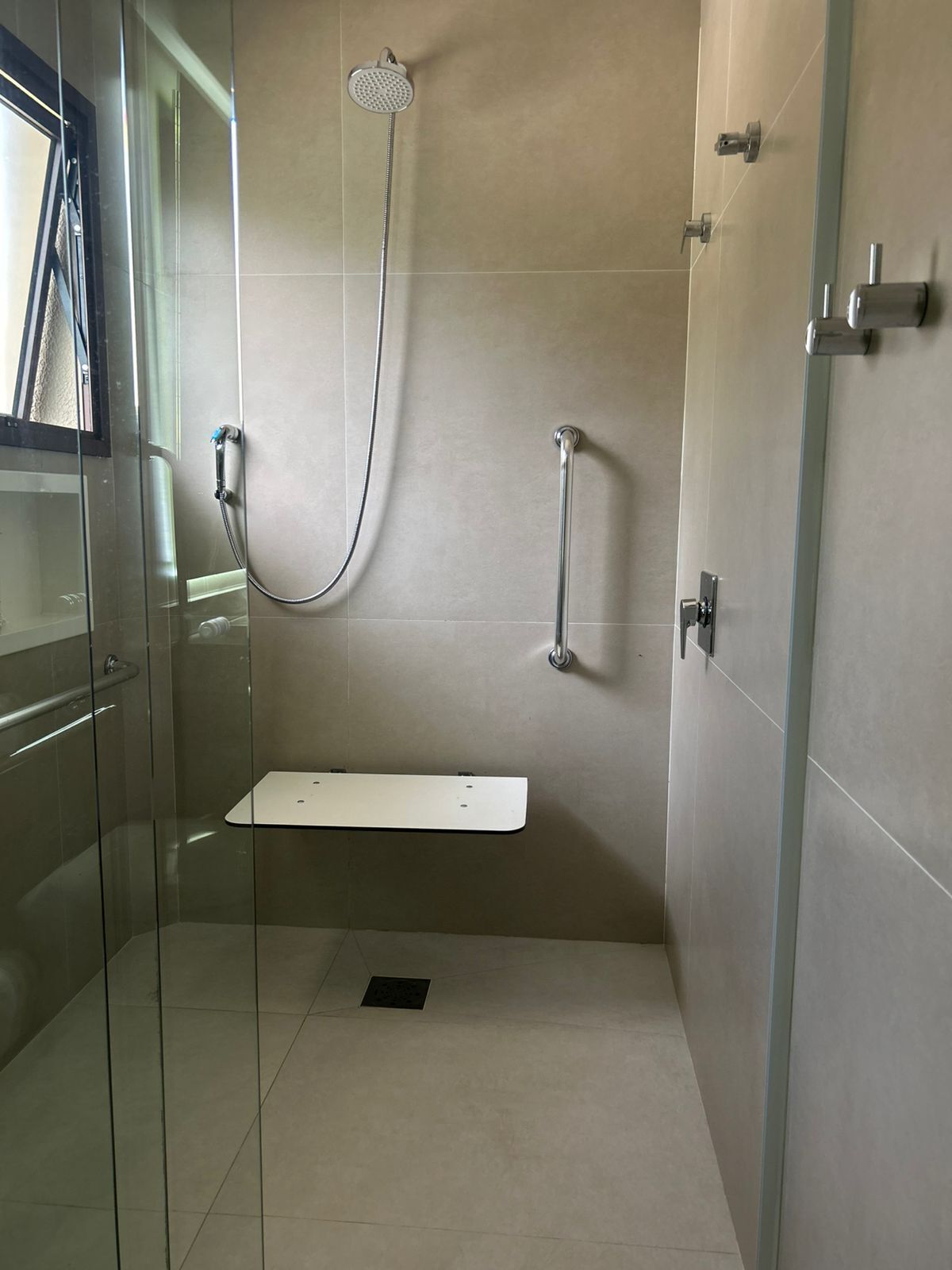 Une cabine de douche moderne dotée d’un pommeau de douche à main, d’un robinet mural et d’un espace de douche délimité par des parois en verre.
