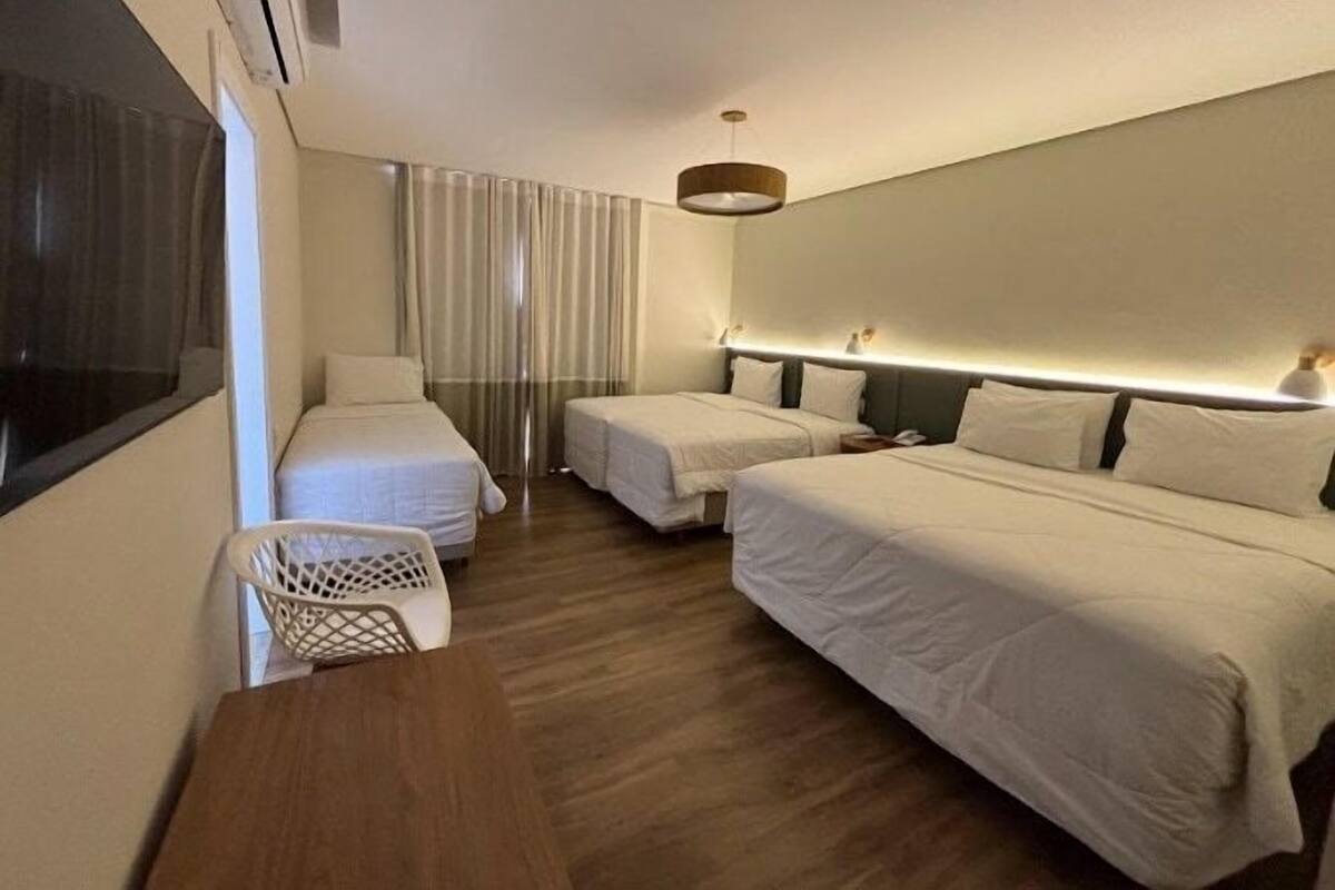 Ein Hotelzimmer mit zwei Einzelbetten, einem Holztisch, einem weißen Stuhl und einem großen Fenster mit Vorhängen.