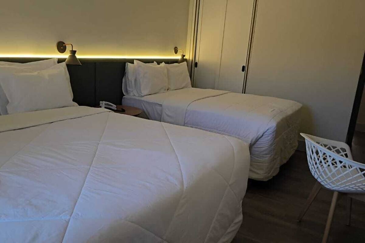 Ein Hotelzimmer mit zwei Betten, einem weißen Sessel und einem Nachttisch mit Lampe.