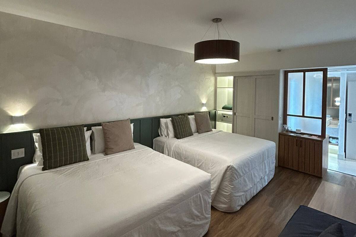 Ein Hotelzimmer mit zwei Betten, einer Couch, Holzboden und einem großen Fenster.