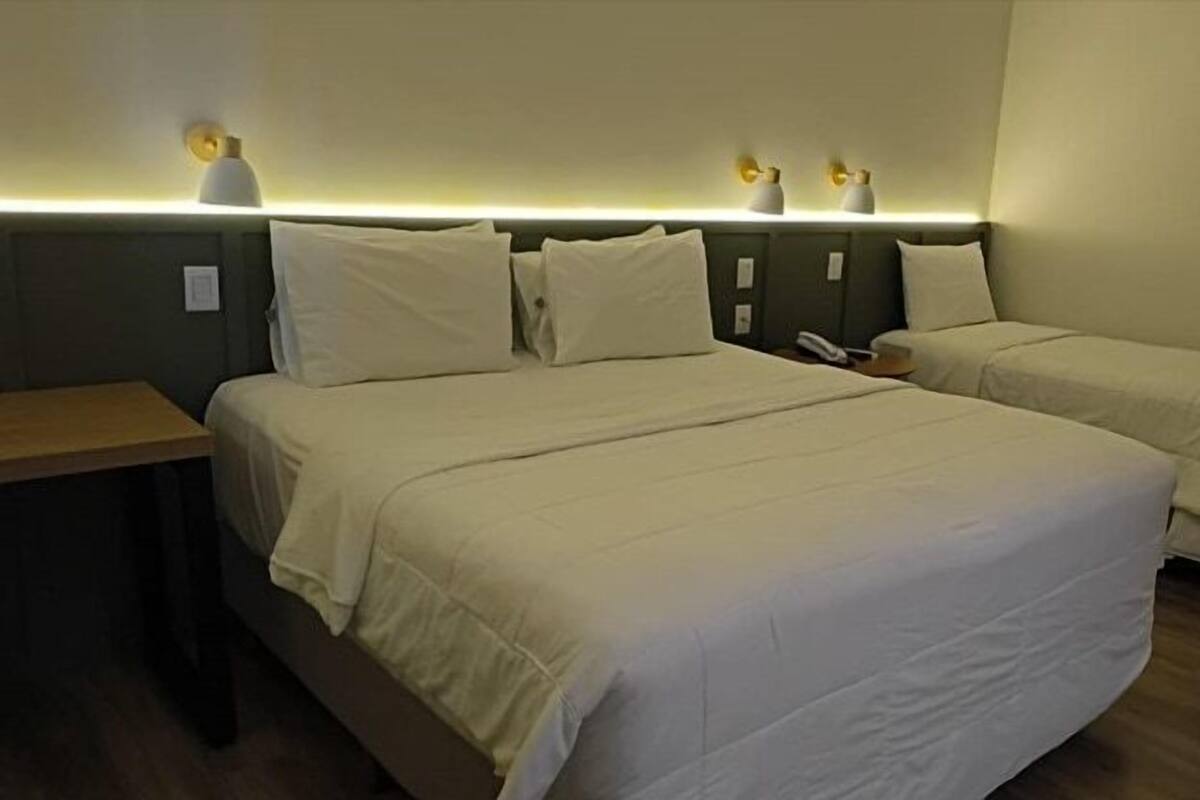 Ein Hotelzimmer mit zwei Einzelbetten, einem Holznachttisch und Wandleuchten.