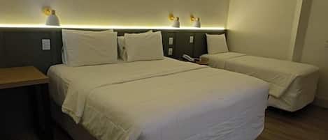 Una habitación de hotel con dos camas individuales, una mesita de noche de madera y lámparas fijadas a la pared.