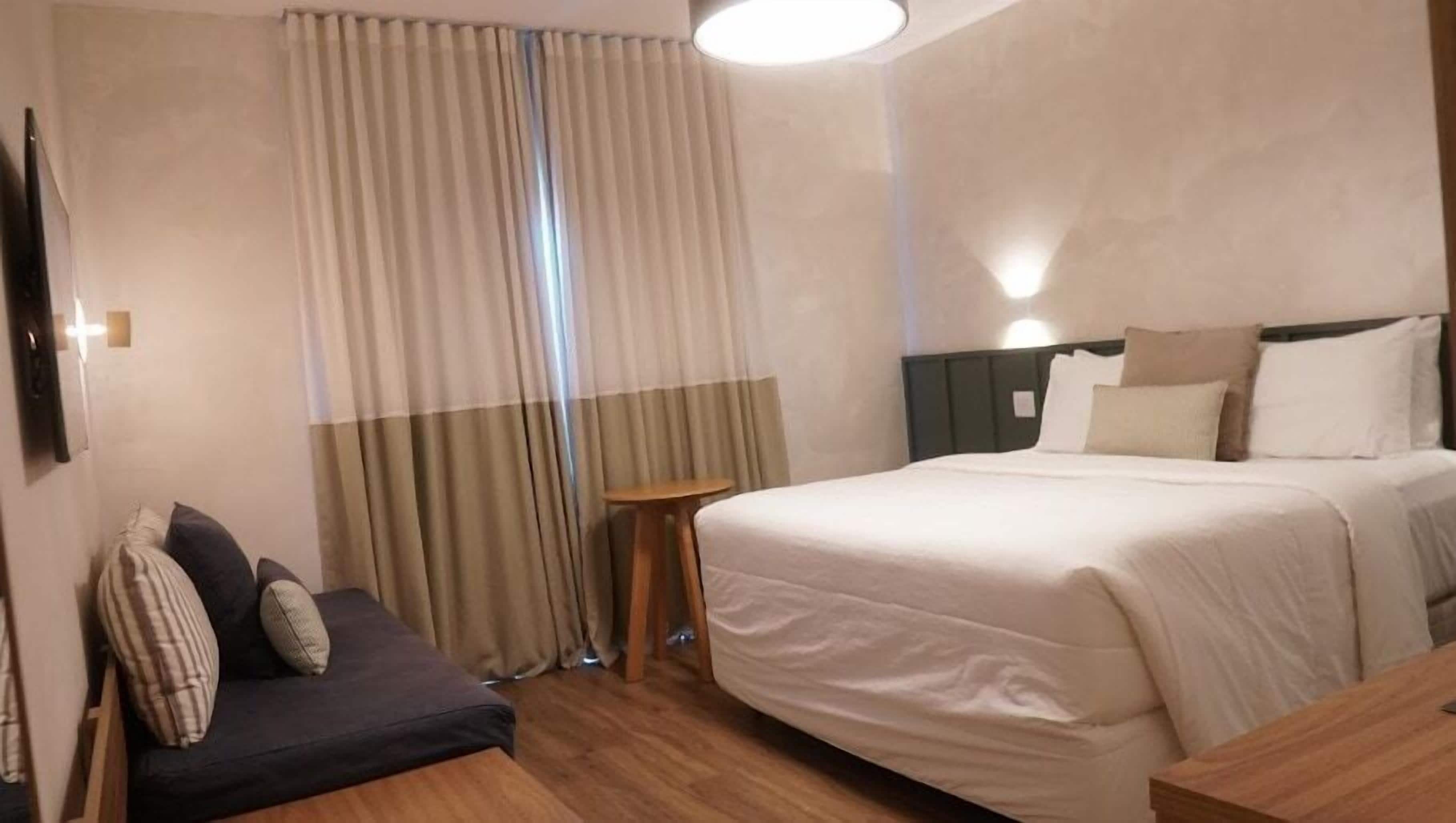 Una camera d'albergo con un letto grande, un tavolino, una poltrona e una tenda.