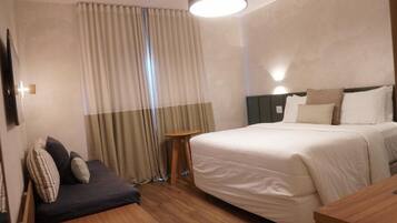 Una camera d'albergo con un letto grande, un tavolino, una poltrona e una tenda.