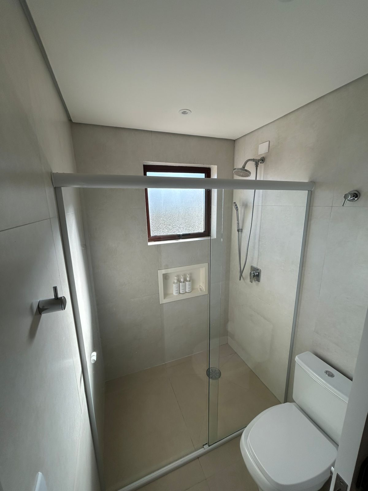 A modern bathroom with a glass shower enclosure, a toilet, and a small window.