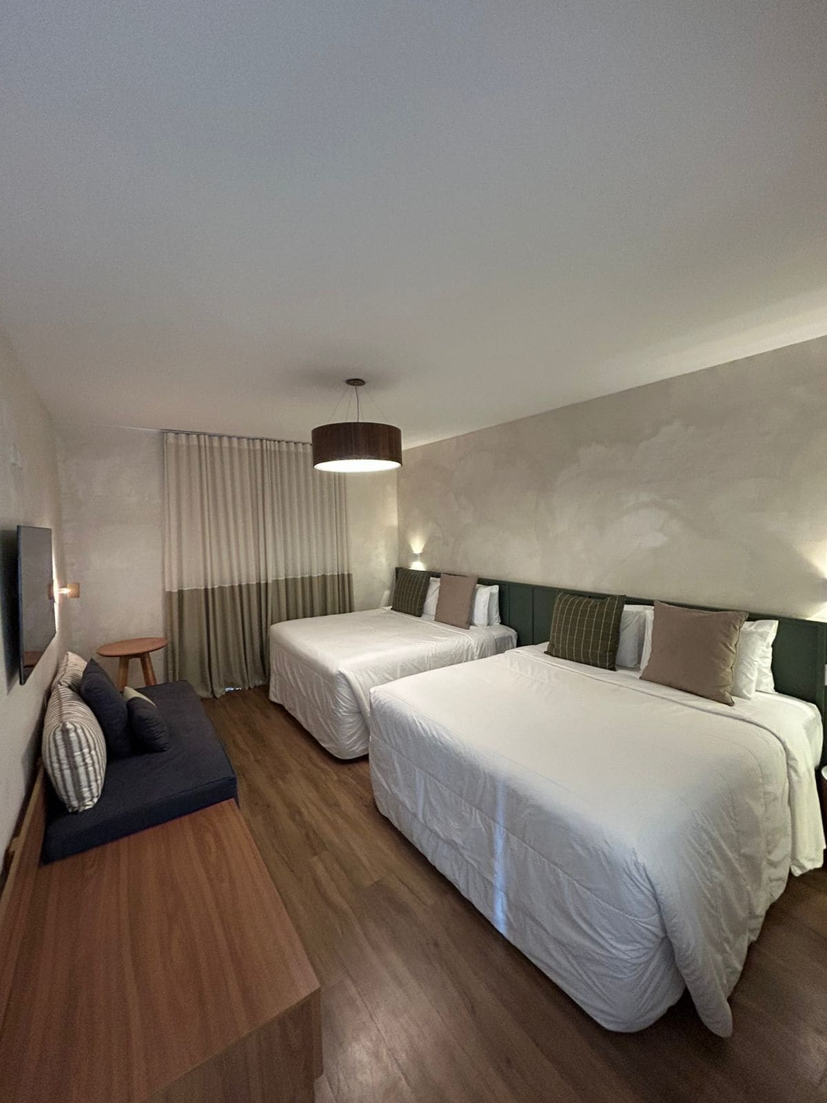 Une chambre d’hôtel avec deux lits simples, un canapé, une télévision et une table d’appoint en bois.