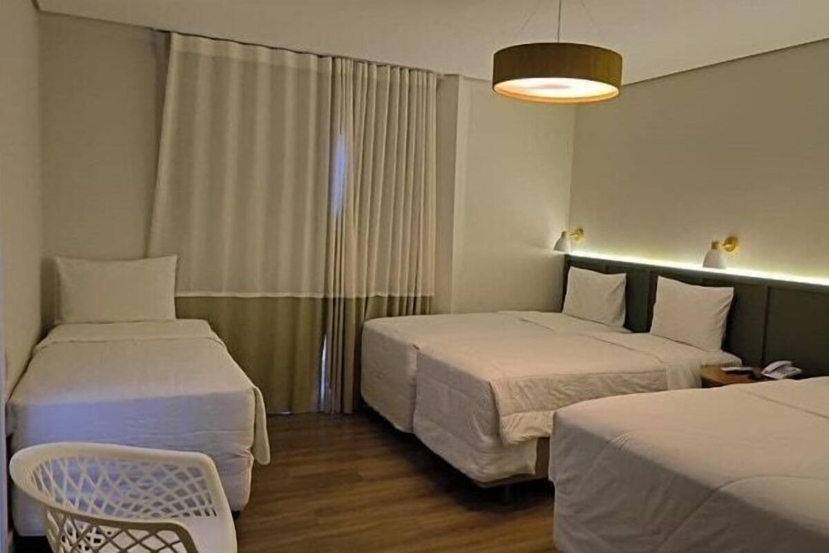 Ein Hotelzimmer mit zwei Betten, einem Sessel und einem Fenster mit Vorhängen.