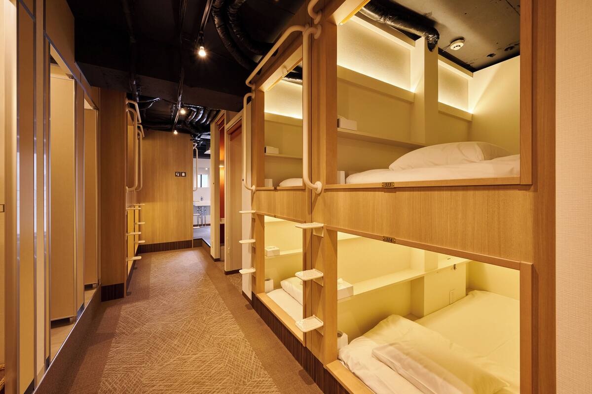 A hotel corridor with bunk beds, wooden walls, and a carpeted floor.