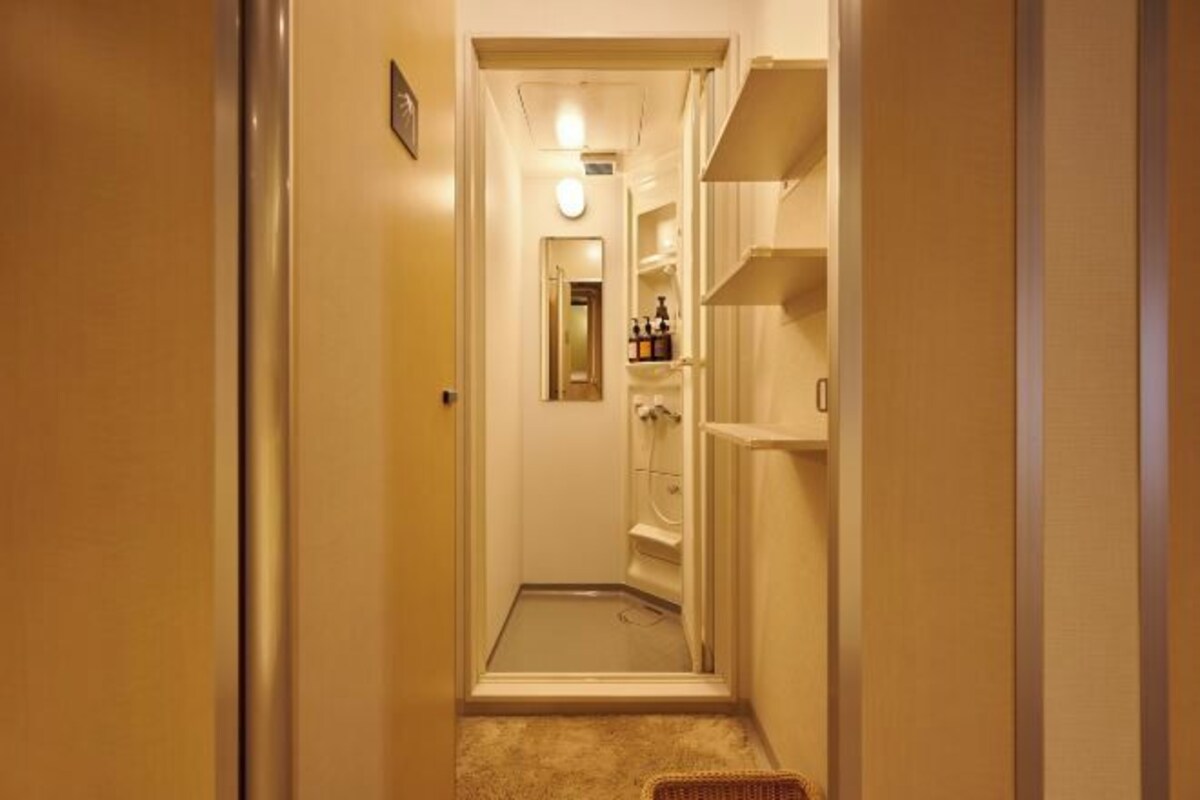 A narrow hallway with a shower area, a door on the left, and shelves on the right.