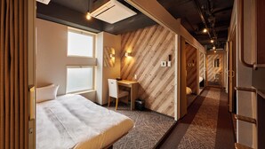 Habitación de hotel con cama, escritorio y vista al pasillo.