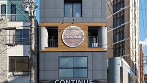 Un hotel moderno llamado "Continue", con un letrero destacado, ventanas amplias y una fachada limpia.