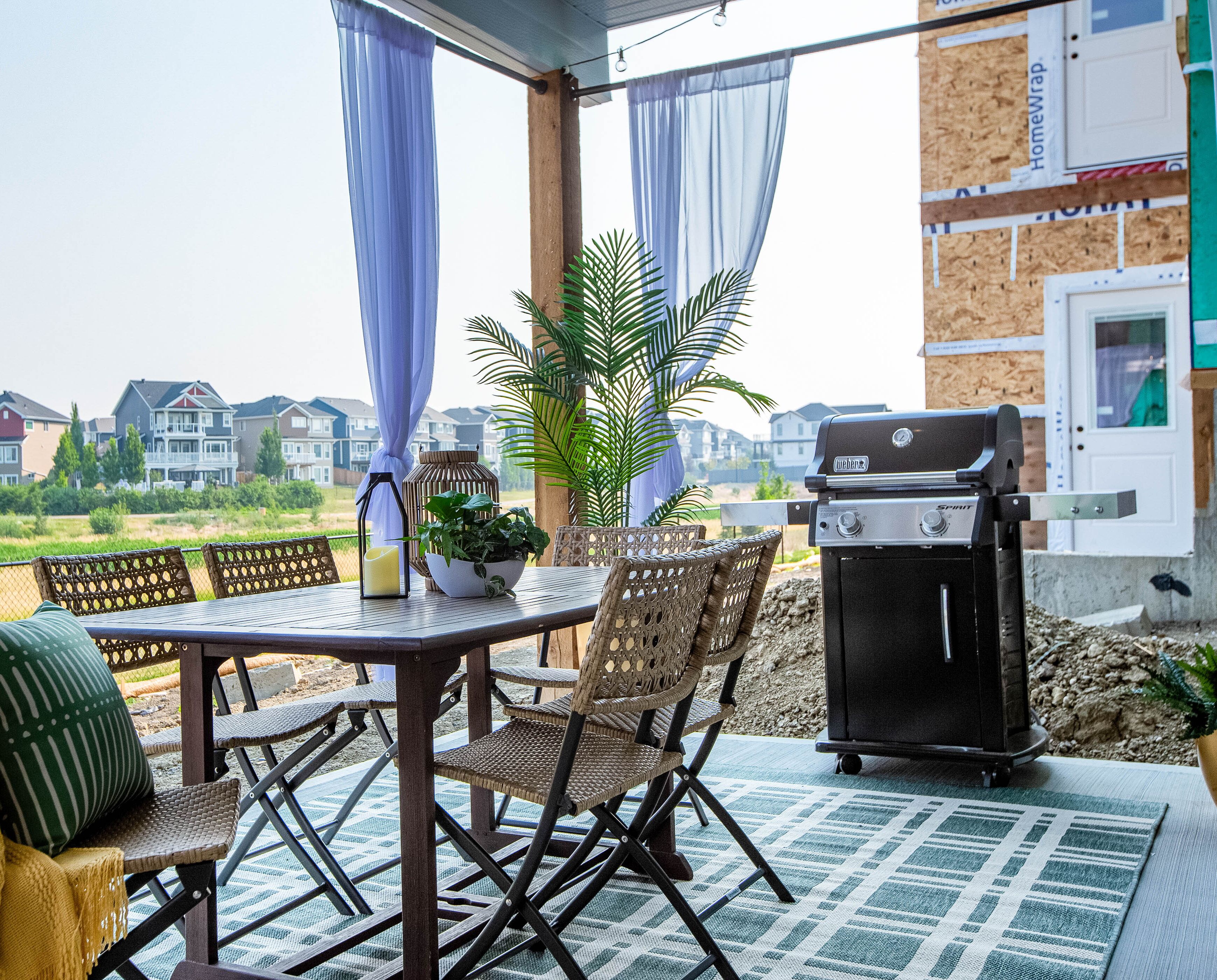 Une terrasse extérieure avec un barbecue, des chaises en osier, une table et une vue sur les maisons au loin.