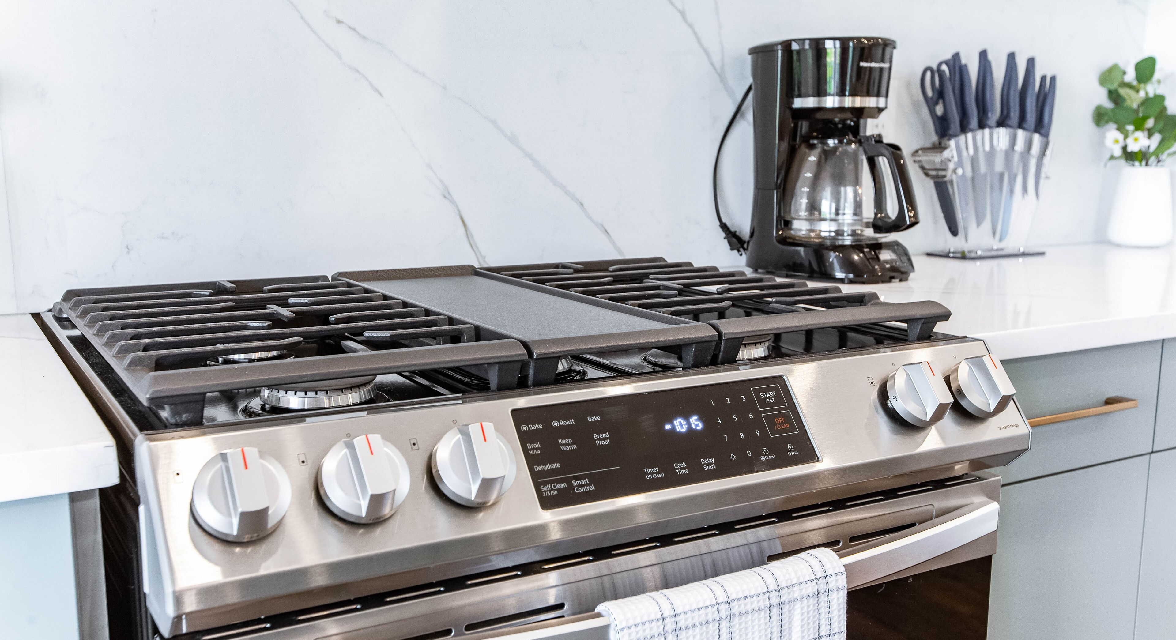 Une cuisine moderne équipée d’une cuisinière en acier inoxydable, d’une machine à café et d’un ensemble de couteaux rangés dans un porte-couteaux.