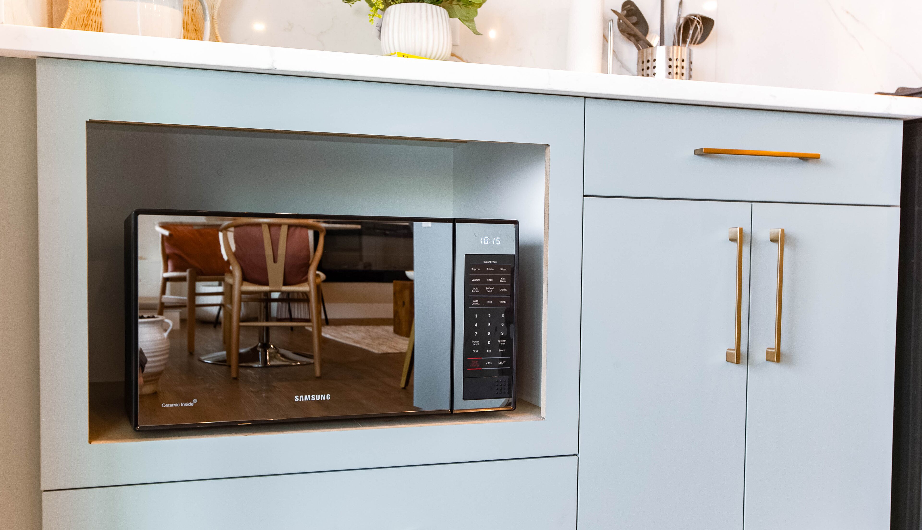 A modern kitchen with a built-in microwave, a chair, and a cabinet with gold handles.