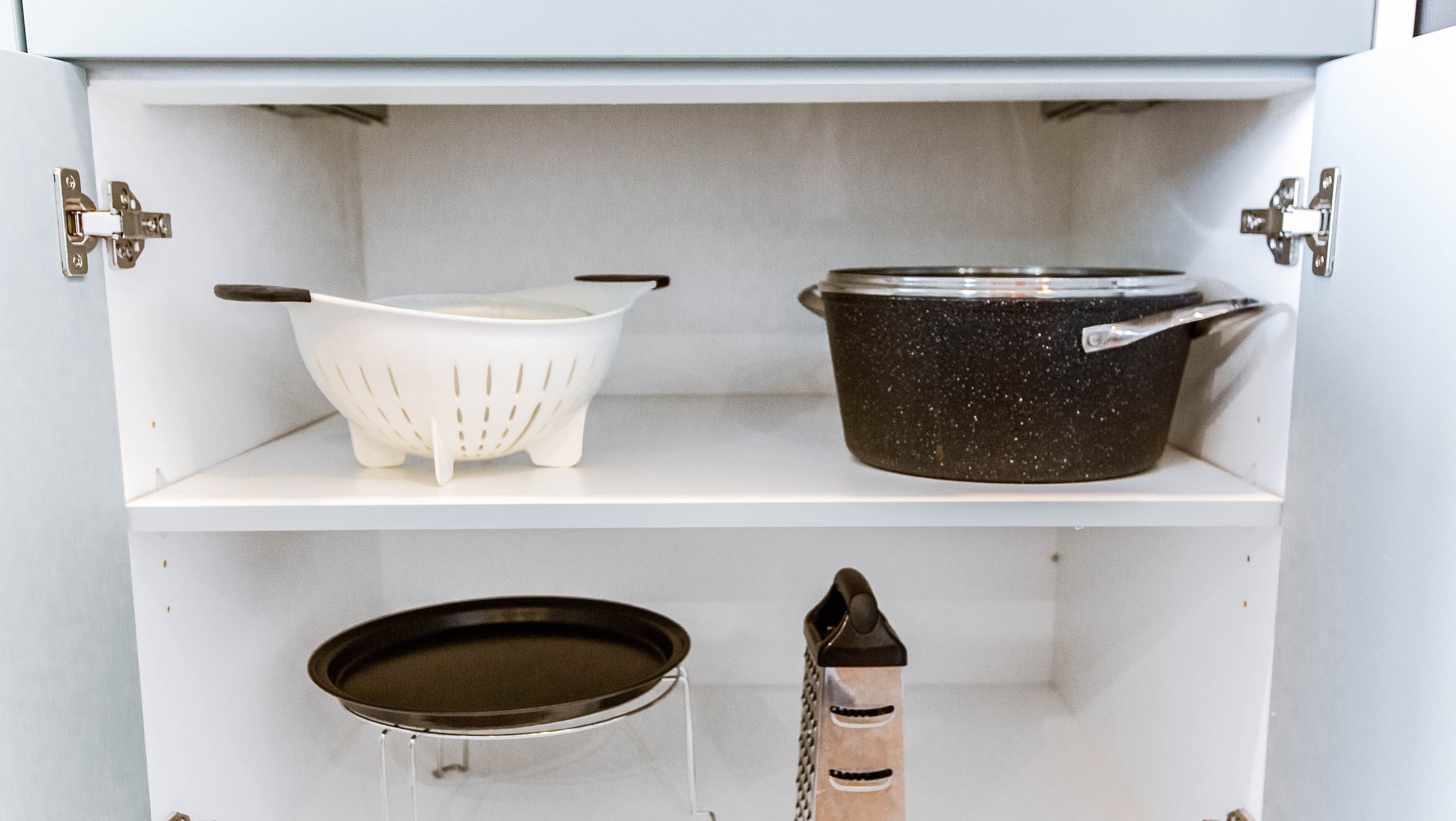 Uno scaffale in cucina con una colander bianca, una pentola nera a pois e una padella nera.