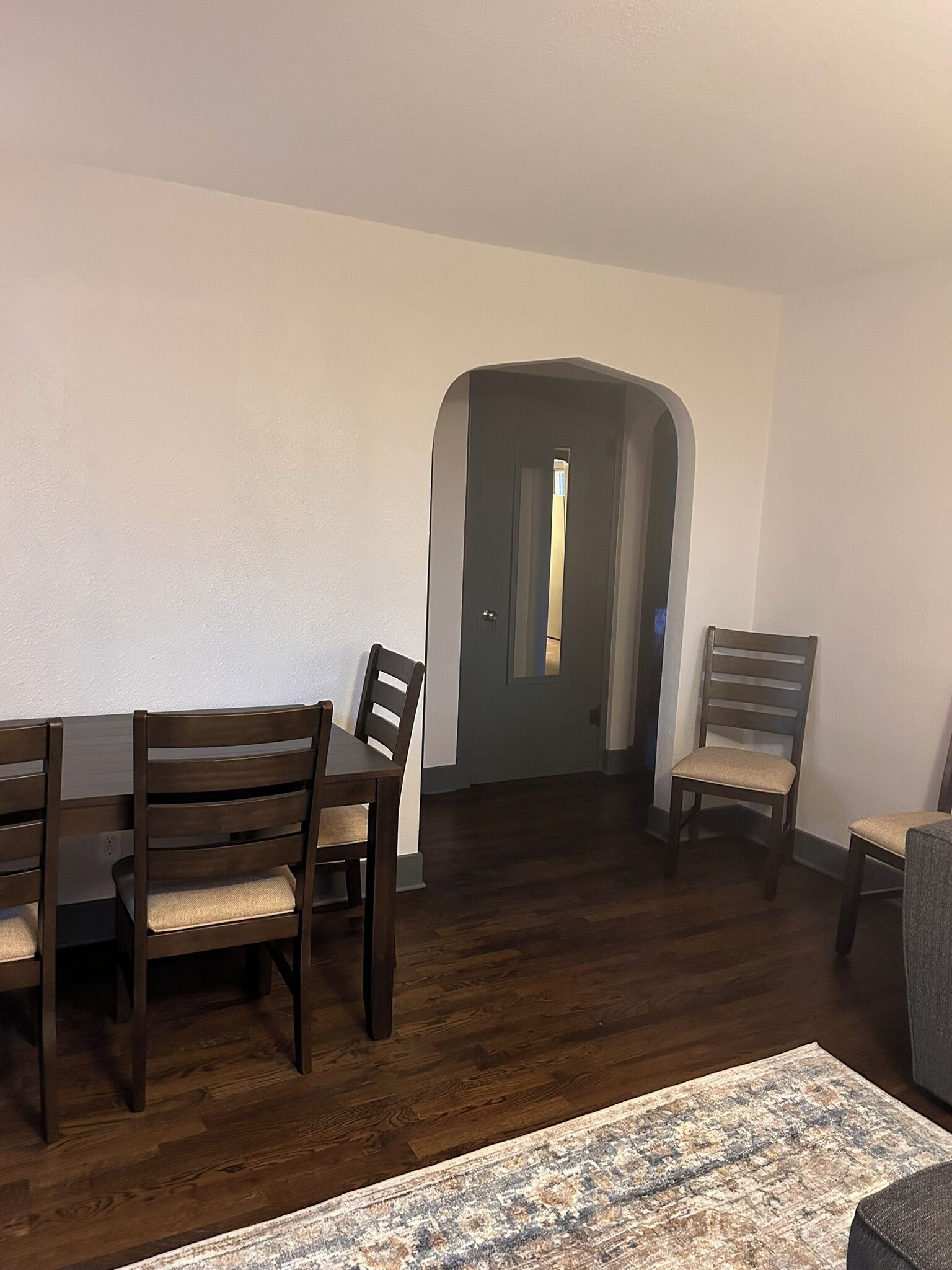 A dining area with a dark wood table and chairs, a patterned rug, and a door leading to another room.