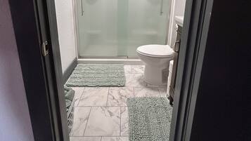 A bathroom with a glass shower door, a toilet, and two green mats on the floor.