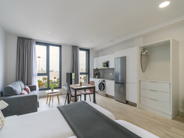 A modern apartment with a bed, a dining area, a kitchen, and a view of the beach.