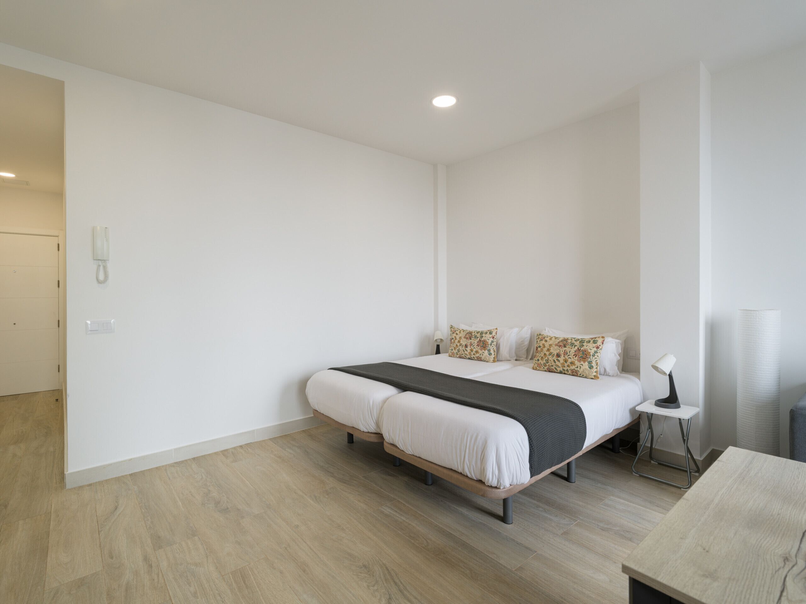 Moderni hotellihuone, jossa on parivuode, yöpöytä, lamppu ja seinässä puhelin.