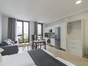 A modern apartment with a bed, a dining area, a kitchen, and a view of the beach.