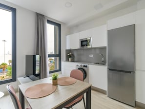 Une cuisine moderne équipée d’un réfrigérateur, d’un four à micro-ondes et d’un four, tous en acier inoxydable. On y trouve une table à manger avec deux sets de table et une plante en pot.