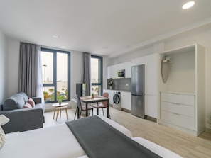 A modern apartment with a bed, a dining area, a kitchen, and a view of the beach.